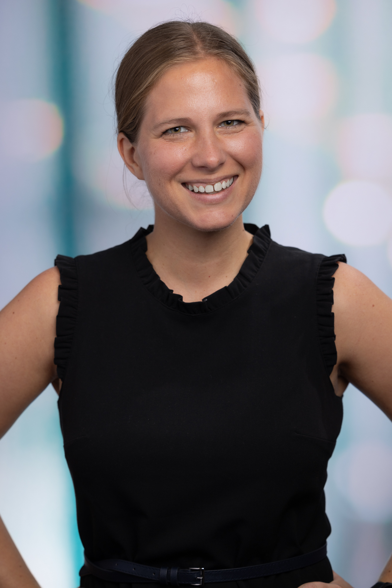 Robyn's headshot (small smile, hair pulled back, black dress, hands on hips)